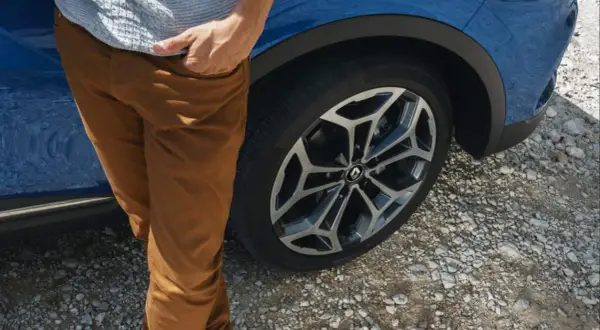 Man med bruna byxor vid en blå Renault Kadjar. Ett hjul syns tydligt, kanske ett tecken på ett Renault Kadjar problem?