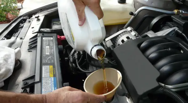Händer häller ny olja i en bilmotor. För att veta hur ofta byta oljefilter, kolla bilens manual.