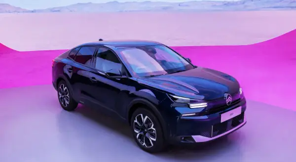 Mörkblå Citroën C4 elbil står på en grå yta med en rosa och lila bakgrund.