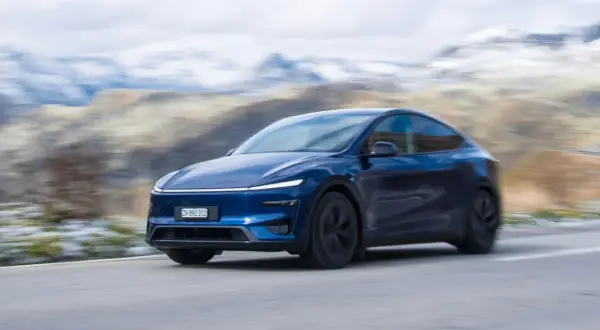 Mörkblå Tesla Model Y Performance kör på en slingrande väg med snöklädda berg i bakgrunden.