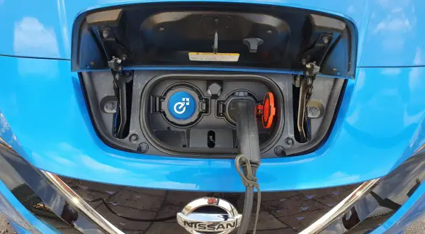 Blue Nissan Leaf with charging port open and cable plugged in.
