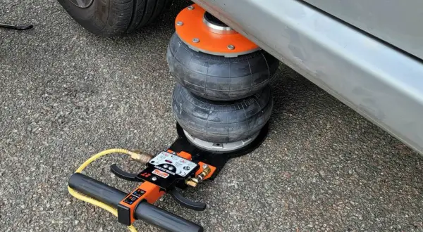 Luftkudde lyfter bilen för däckbyte. En domkraft med slang och handtag syns.