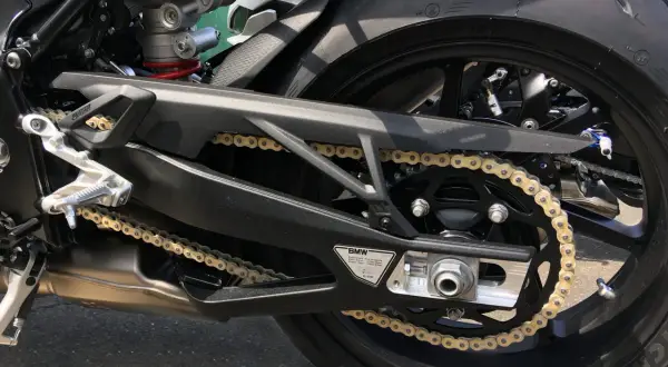 Detaljbild på en motorcykels bakparti med ett gyllene kedjespel mc som löper över ett svart drev. Däcket är ett Michelin.
