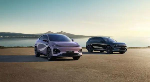 Två XPeng SUV:ar, en lila och en svart, står vid en sjö med berg i bakgrunden.