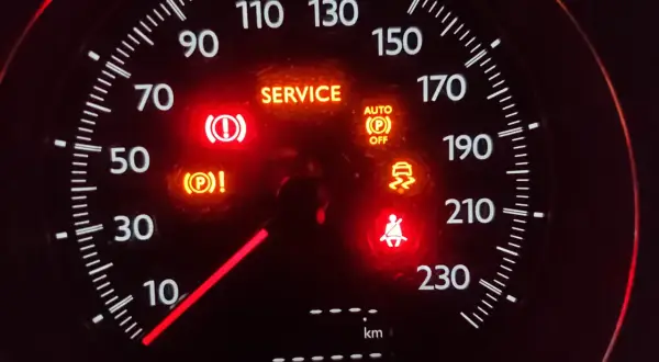 Car dashboard with multiple illuminated warning lights: SERVICE, brake, traction control, seatbelt, and auto park off.
