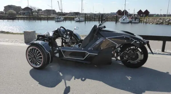 Svart, futuristisk motorcykel på b-kort står vid en hamn med segelbåtar.