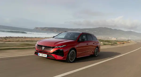 Röd Peugeot 308 kombi kör längs en kustväg. Inga problem med denna bil, bara en vacker vy.