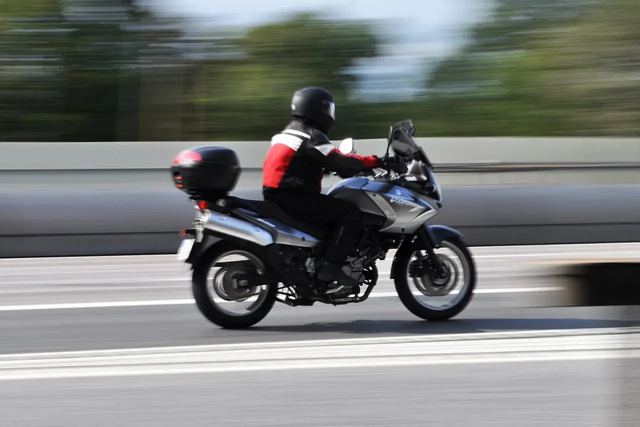 En förare på en pansar mc susar fram på en motorväg, med träd som suddiga gröna streck i bakgrunden.