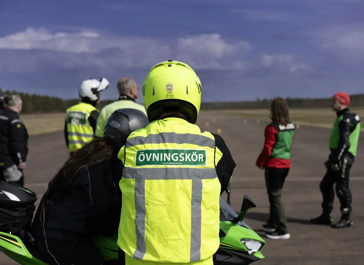 Motorcykelutbildning pågår. En handledare med texten "Övningskör" på västen står redo. Frågan om hur många elever en handledare får ha är relevant för säkerheten.