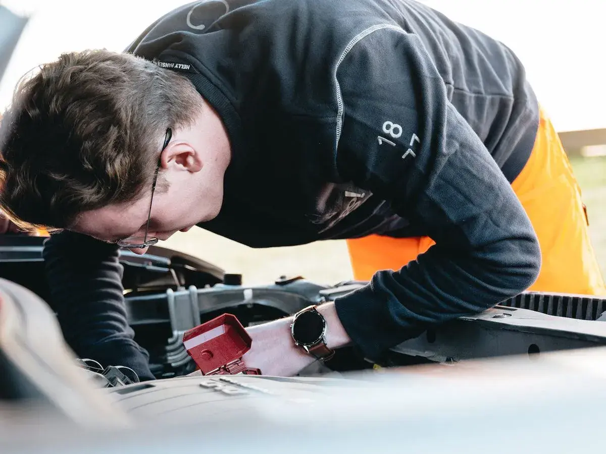 Man med glasögon böjd över bilmotorn, kanske för att fixa det brummande ljudet från bilen.