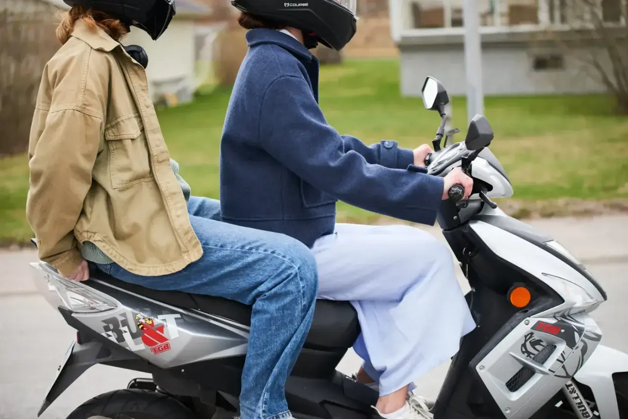 Två personer på moped, en bakom den andra. Följer 30 moped regler för en säker tur.