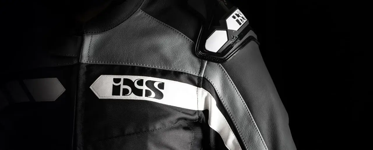 Detaljer på en svart och grå ixs motorcykeljacka med vita logotyper.