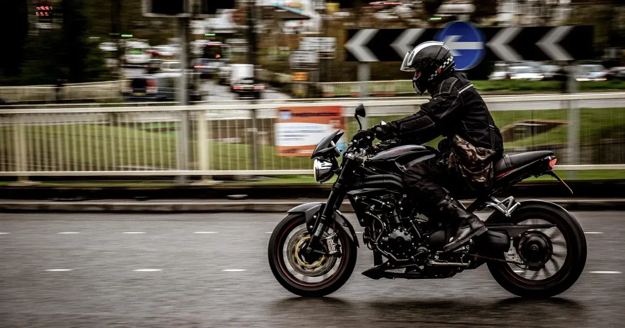 Motorcyklist i full fart på en svart motorcykel, med en praktisk tubhalsduk runt halsen för att skydda mot vinden.