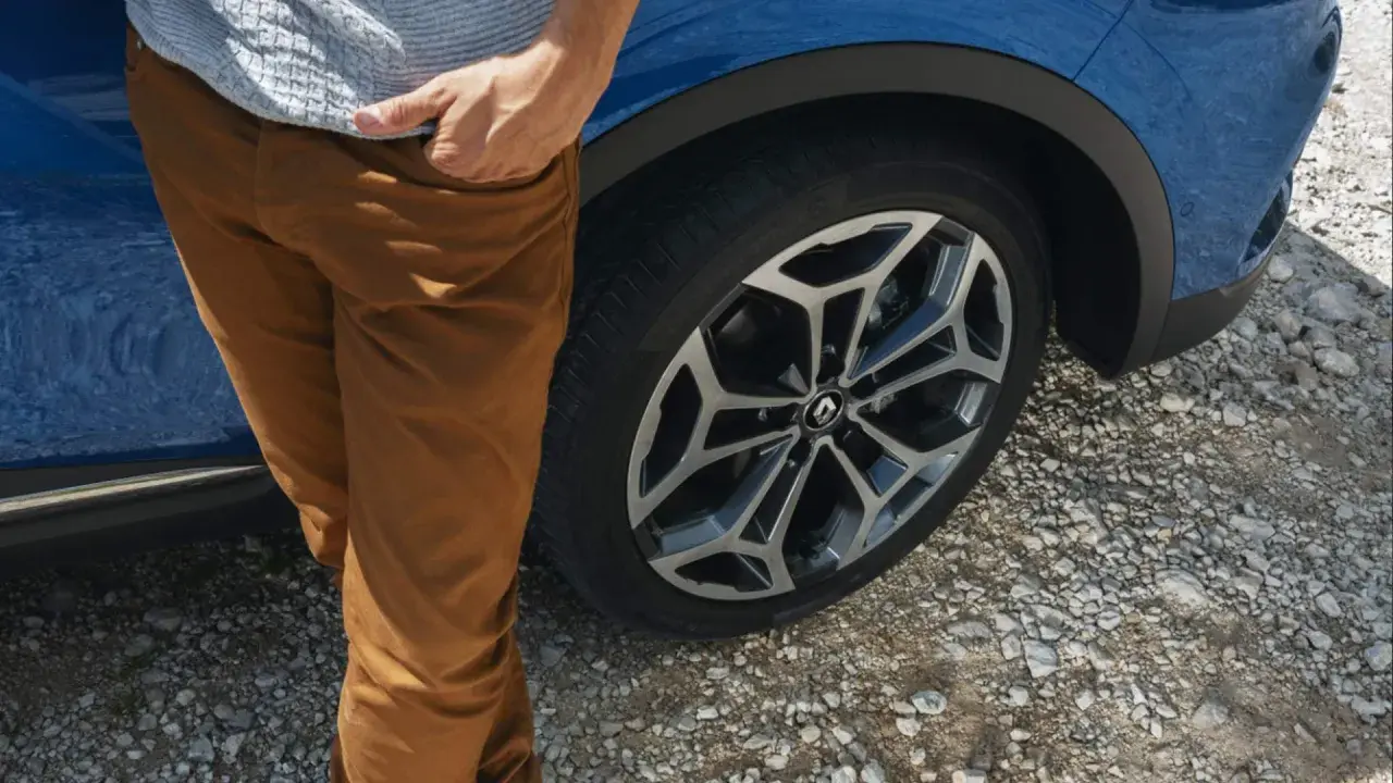 Man med bruna byxor vid en blå Renault Kadjar. Ett hjul syns tydligt, kanske ett tecken på ett Renault Kadjar problem?