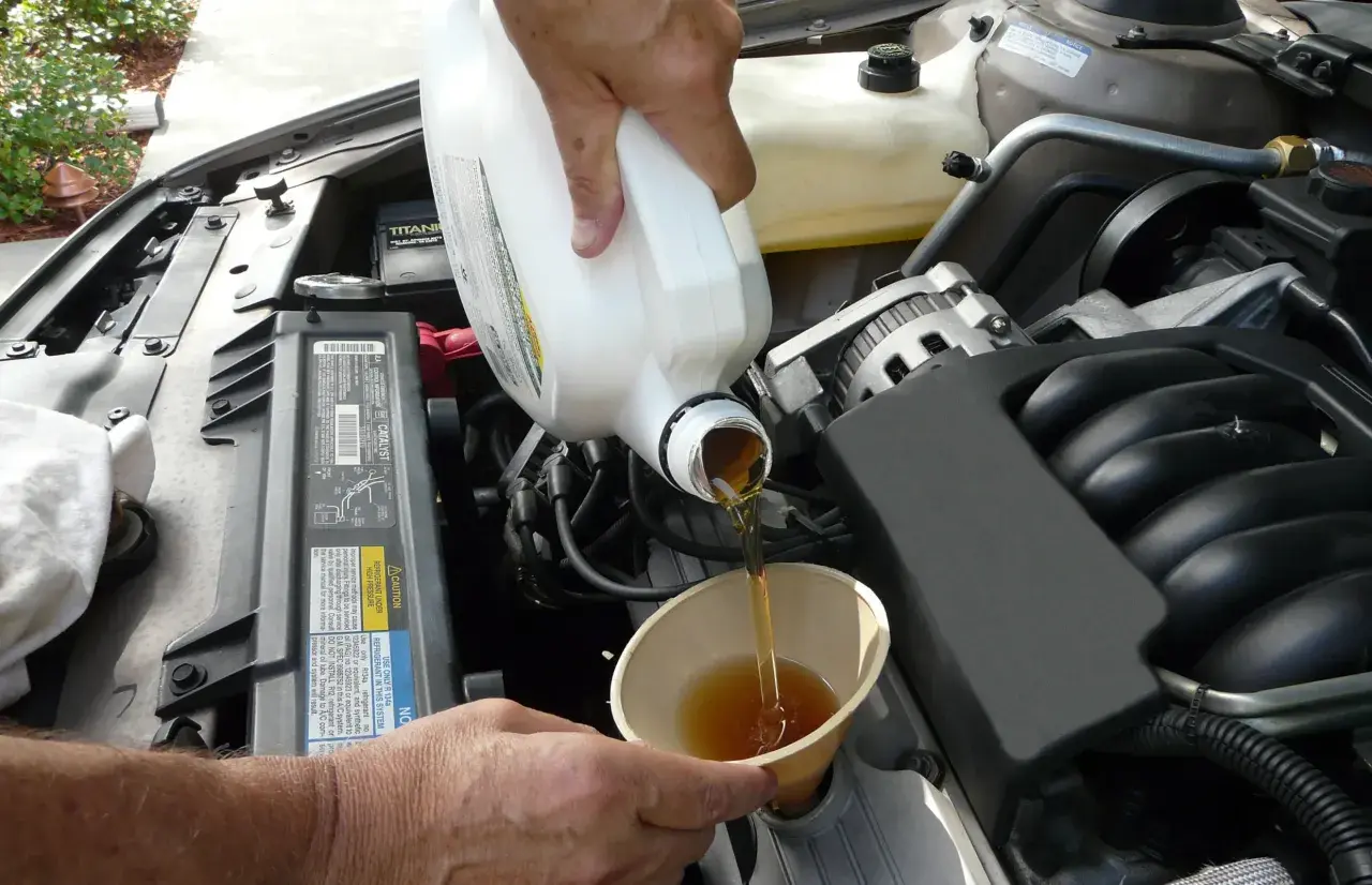 Händer häller ny olja i en bilmotor. För att veta hur ofta byta oljefilter, kolla bilens manual.