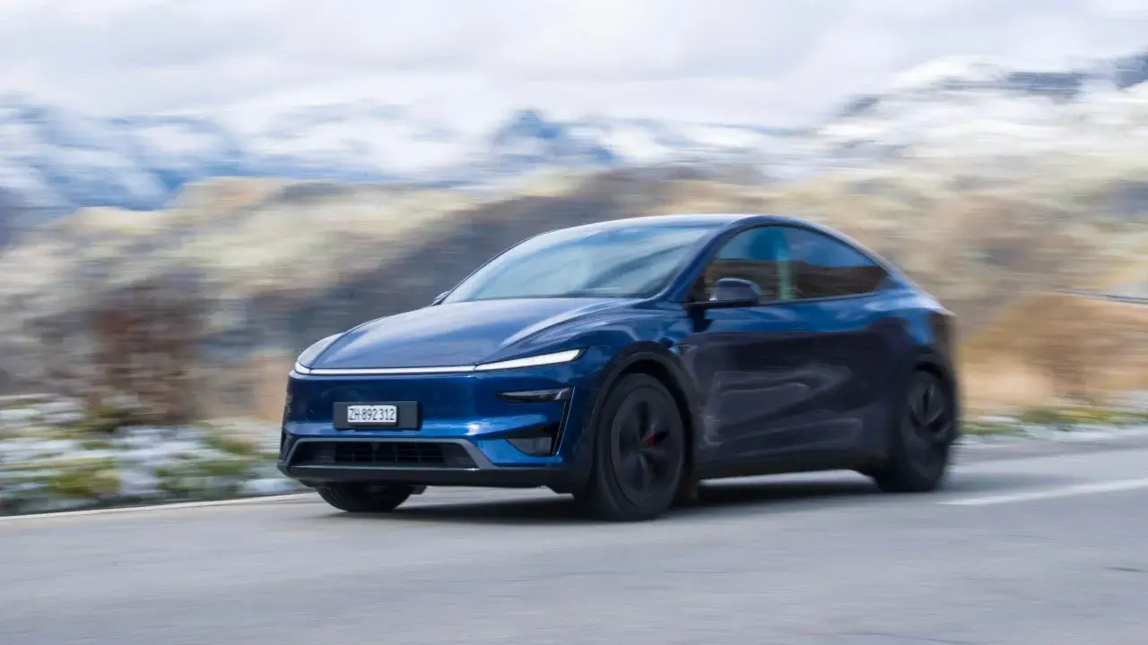 Mörkblå Tesla Model Y Performance kör på en slingrande väg med snöklädda berg i bakgrunden.