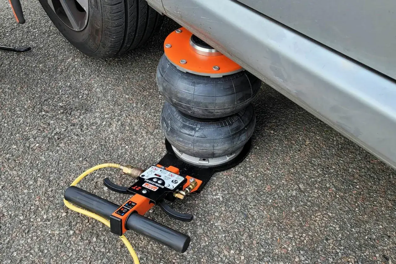 Luftkudde lyfter bilen för däckbyte. En domkraft med slang och handtag syns.