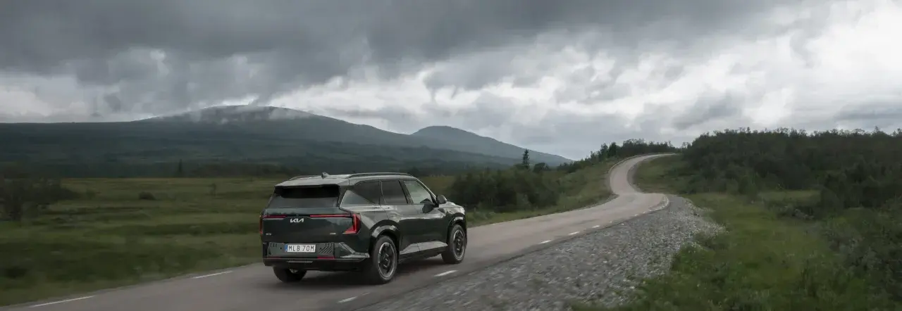 Mörkgrön elbil kör på en slingrande väg genom ett bergigt landskap med molniga himlar. Kanske en försmak av elbilspremie 2026.