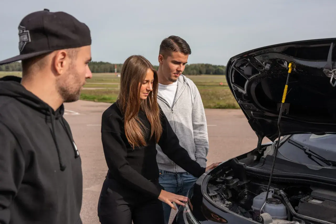 Tre unga vuxna tittar på en bilmotor. Kanske de funderar på om man måste gå handledarkurs för att få köra.