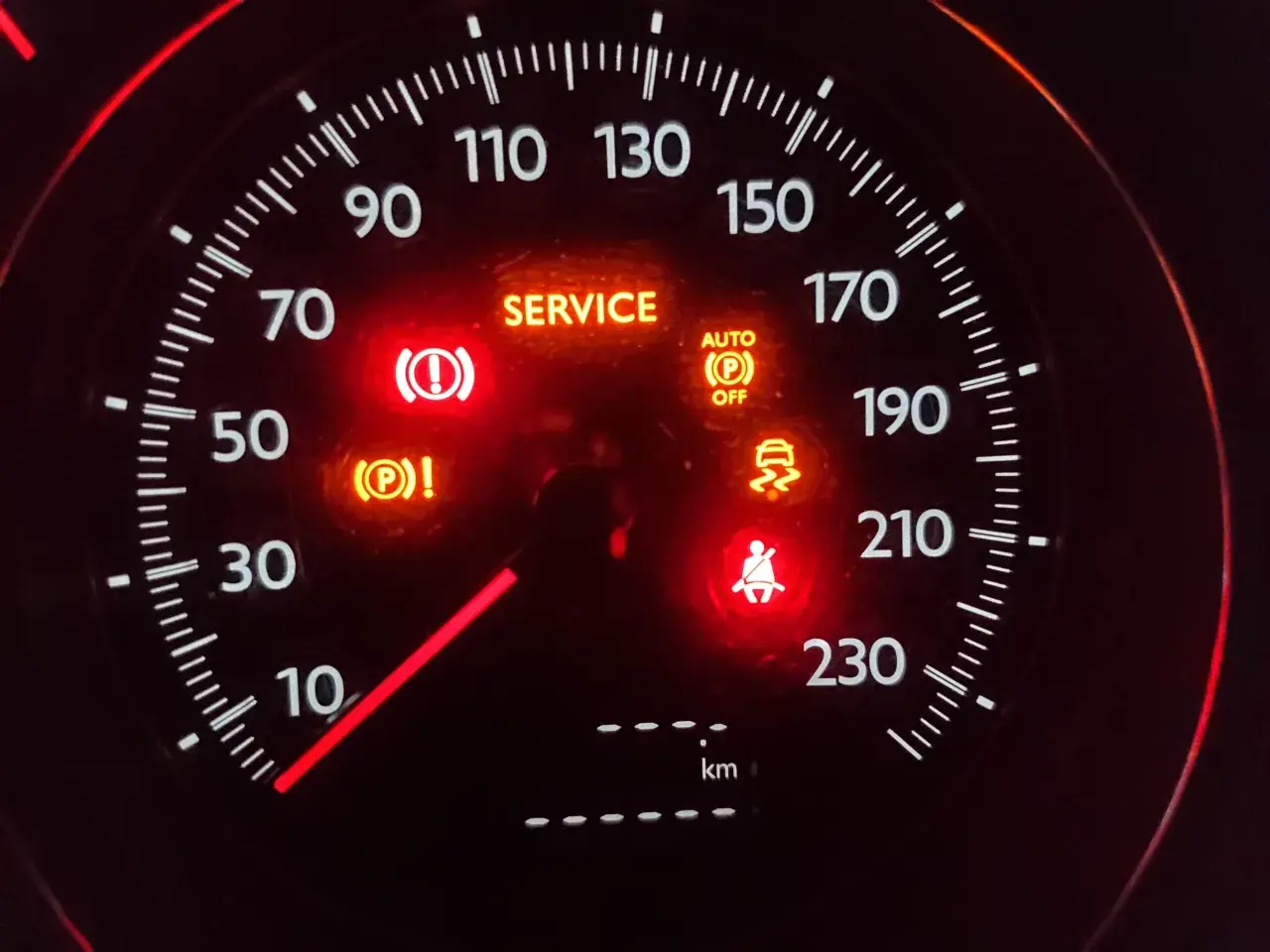 Car dashboard with multiple illuminated warning lights: SERVICE, brake, traction control, seatbelt, and auto park off.