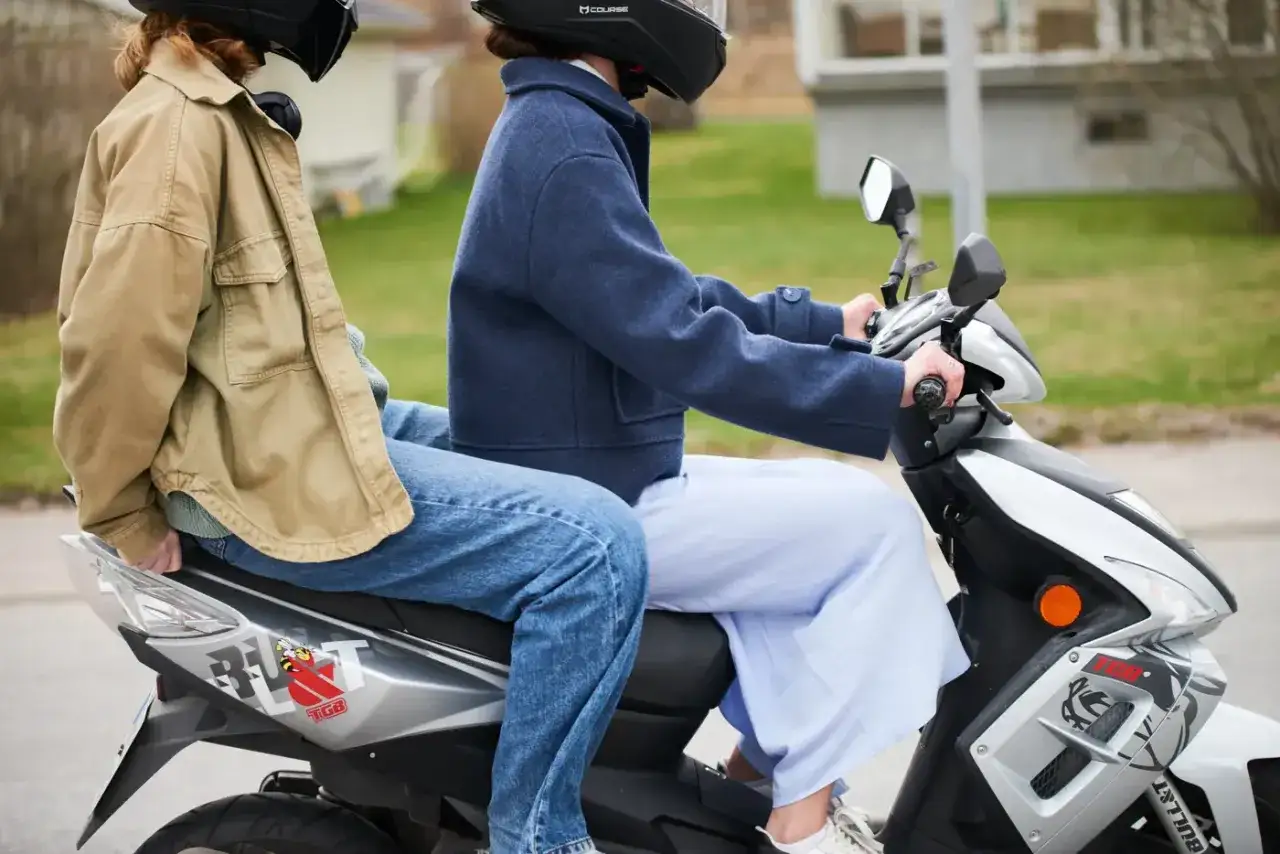 Två personer på moped, en bakom den andra. Kanske är det dags att kolla upp 30 moped regler innan nästa tur.