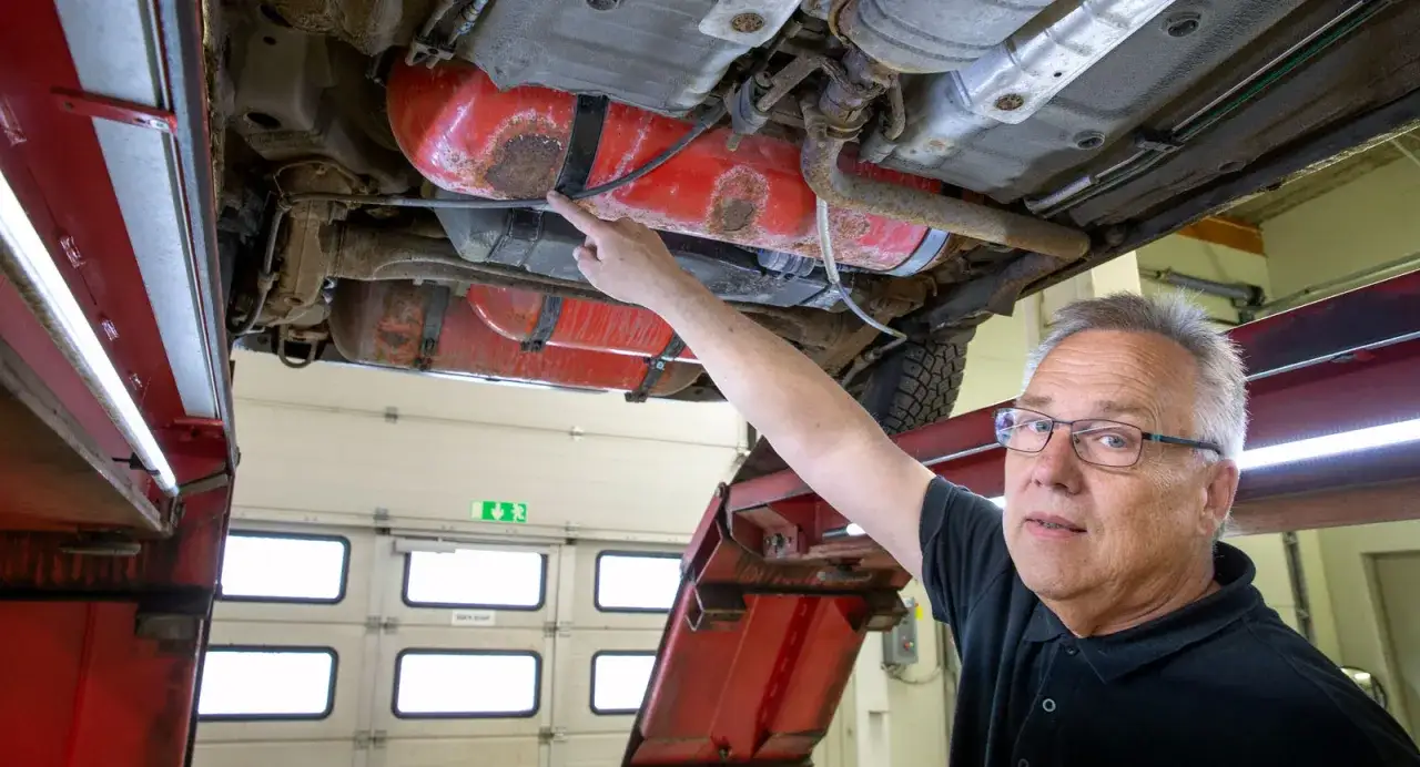 Mekaniker pekar p&aring; en rostig tank under en lpg bil.