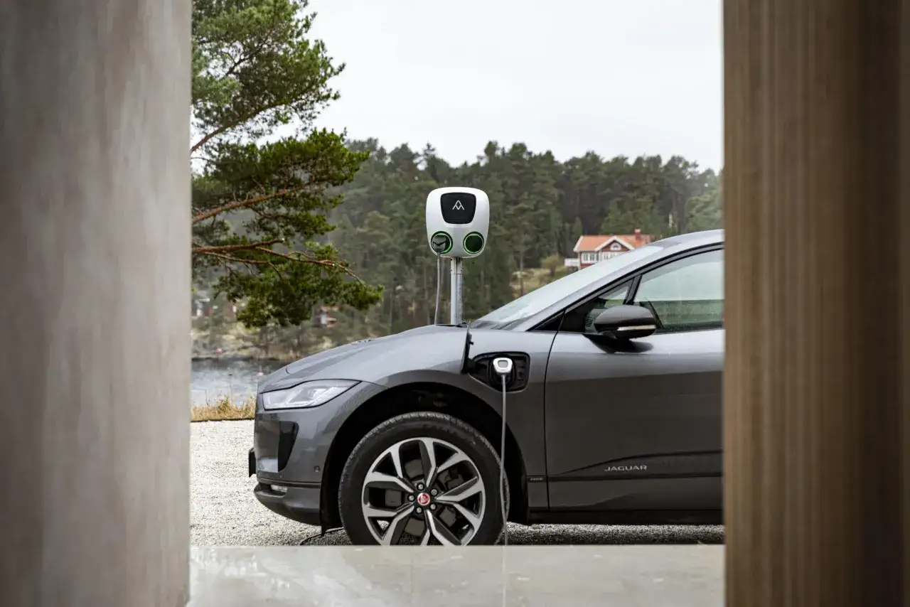 Grå elbil laddas vid en laddstation i vacker svensk natur. Snart redo att ladda elbil 100 procent för äventyr.