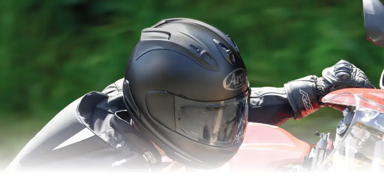 En motorcyklist med en matt svart Arai hj&auml;lm och svarta handskar h&aring;ller i styret p&aring; en r&ouml;d motorcykel.