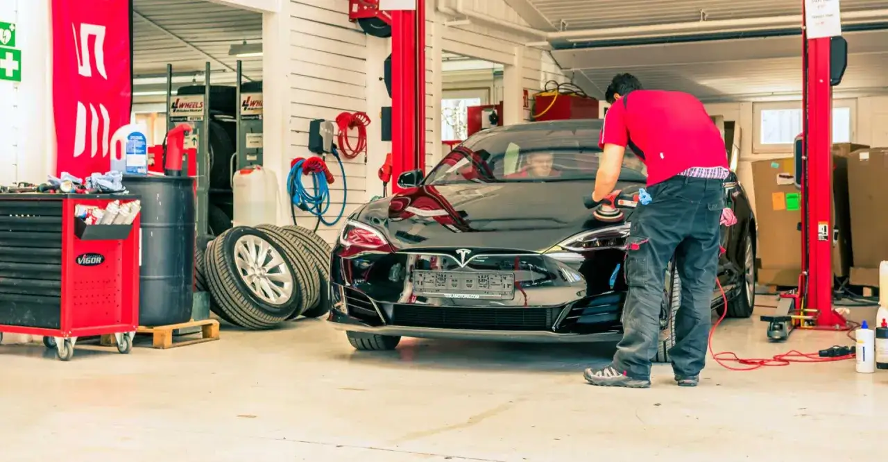 En tekniker polerar en svart Tesla i en verkstad. Kanske en del av ett Tesla service pris.