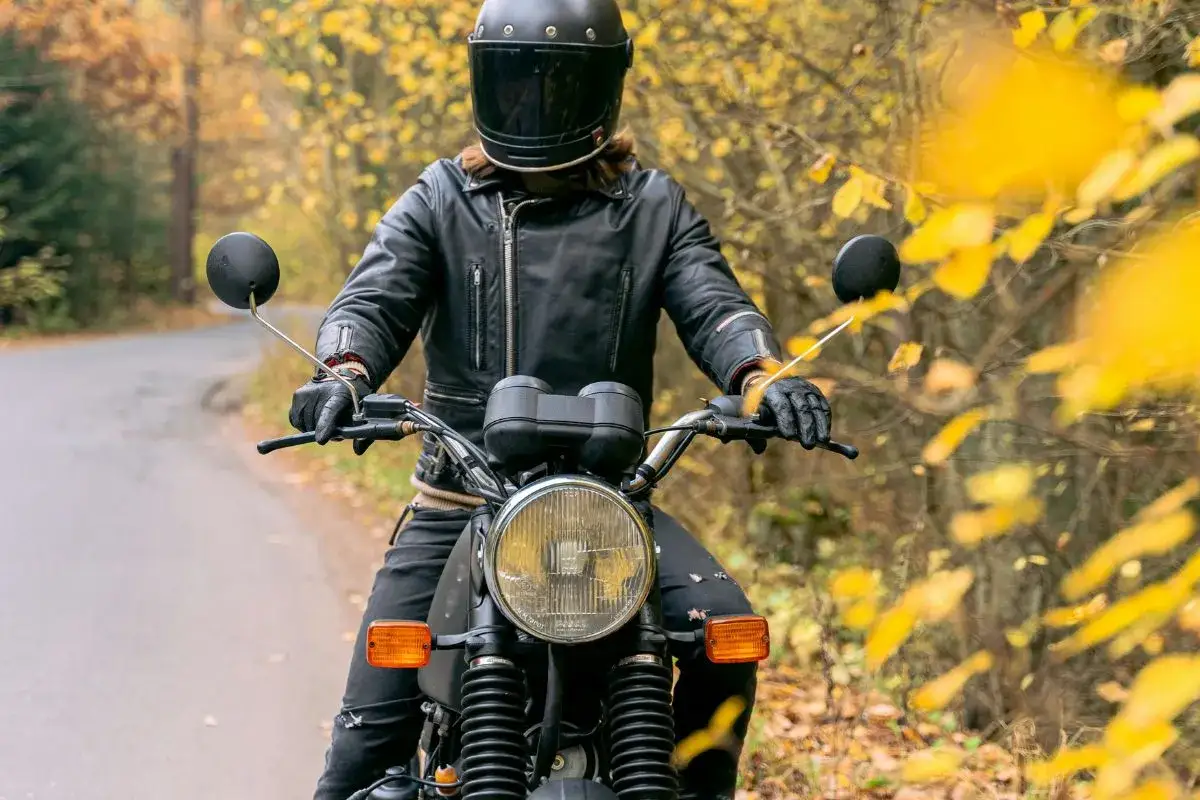 En person i l&auml;derjacka och hj&auml;lm k&ouml;r motorcykel p&aring; en v&auml;g kantad av h&ouml;stf&auml;rger. K&auml;nslan av frihet och a1 motorcykel hastighet infinner sig.