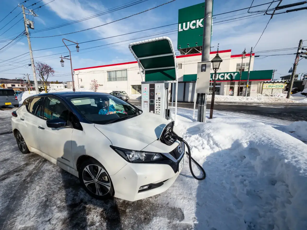 Vit Nissan Leaf 40 kWh laddas vid en laddstation i snöig miljö.
