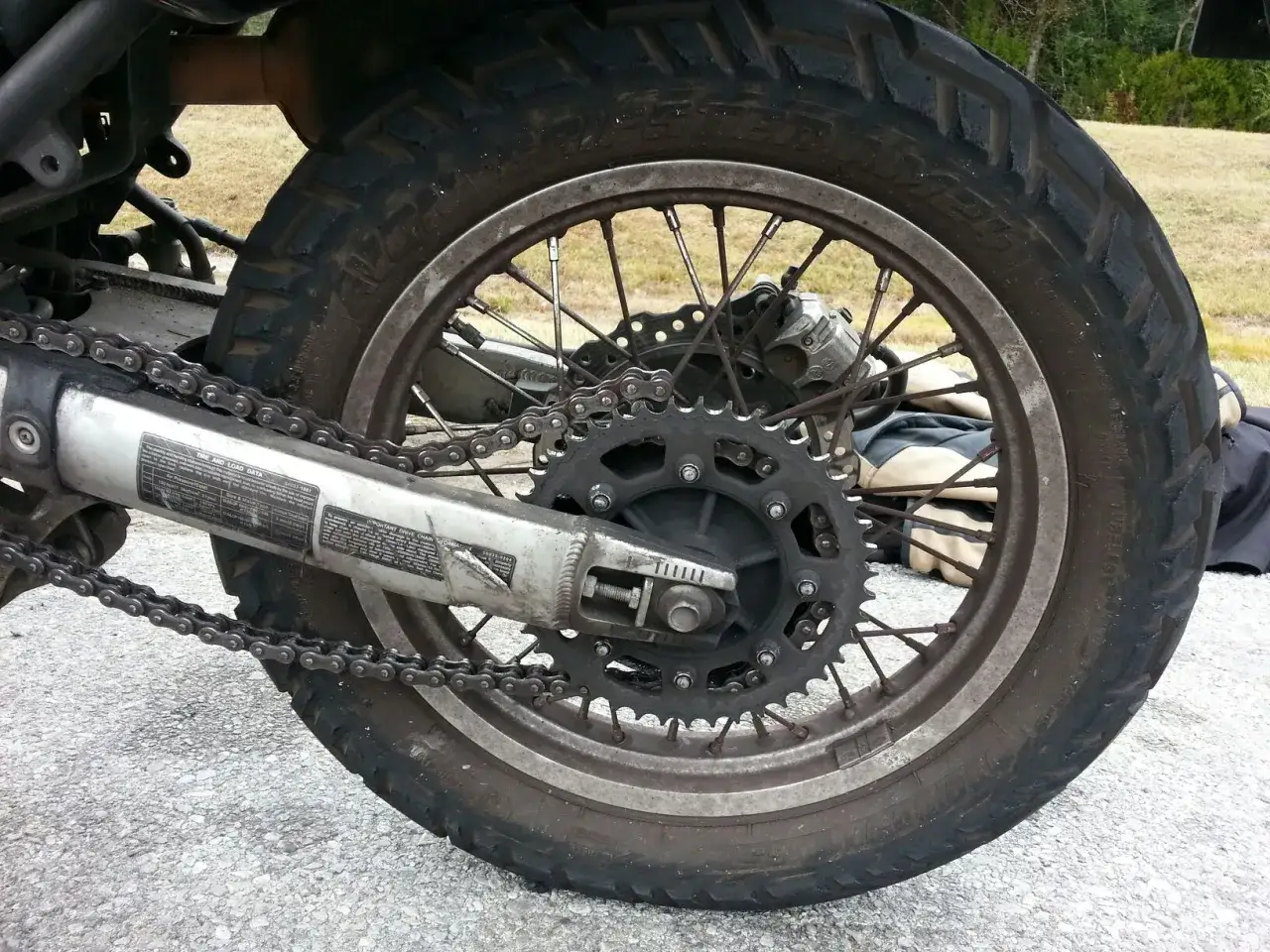 Motorcykelns kedjespel med kedja, drev och bakhjul. Däcket är grovmönstrat, redo för äventyr.
