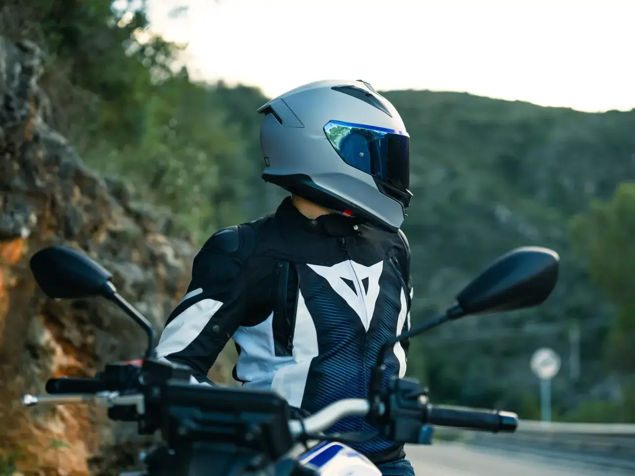 Motorcyklist i en snygg Dainese skinnjacka med vit logga, redo för en tur på vägen.