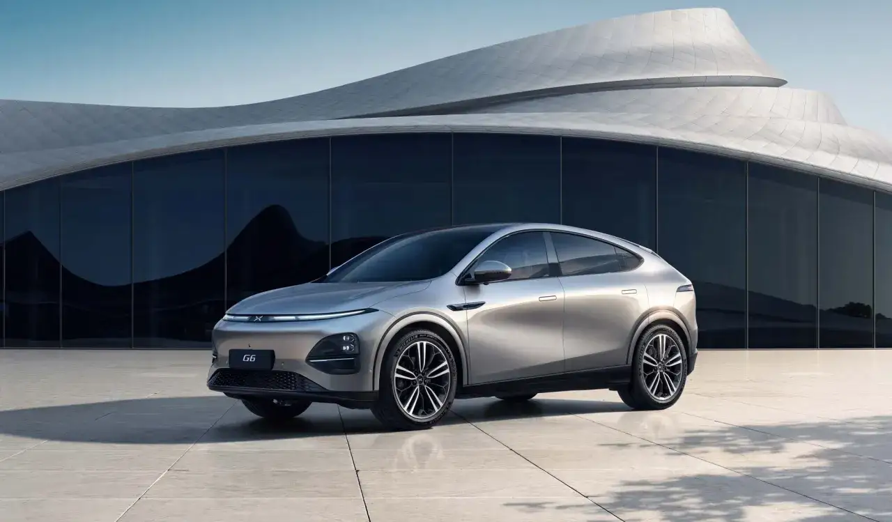 Silver XPENG G6 SUV parkerad framför en modern byggnad med böjda linjer.