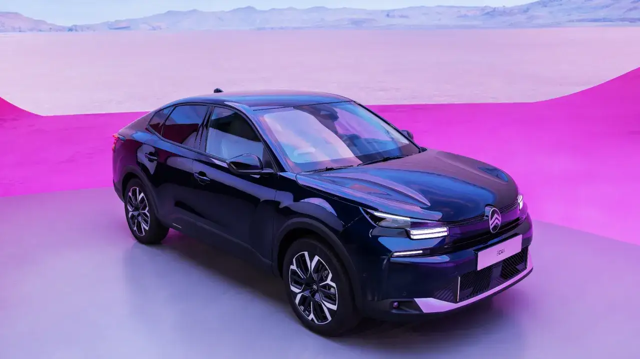 M&ouml;rkbl&aring; Citro&euml;n C4 elbil st&aring;r p&aring; en ljusgr&aring; yta med en rosa bakgrund och berg i fj&auml;rran.