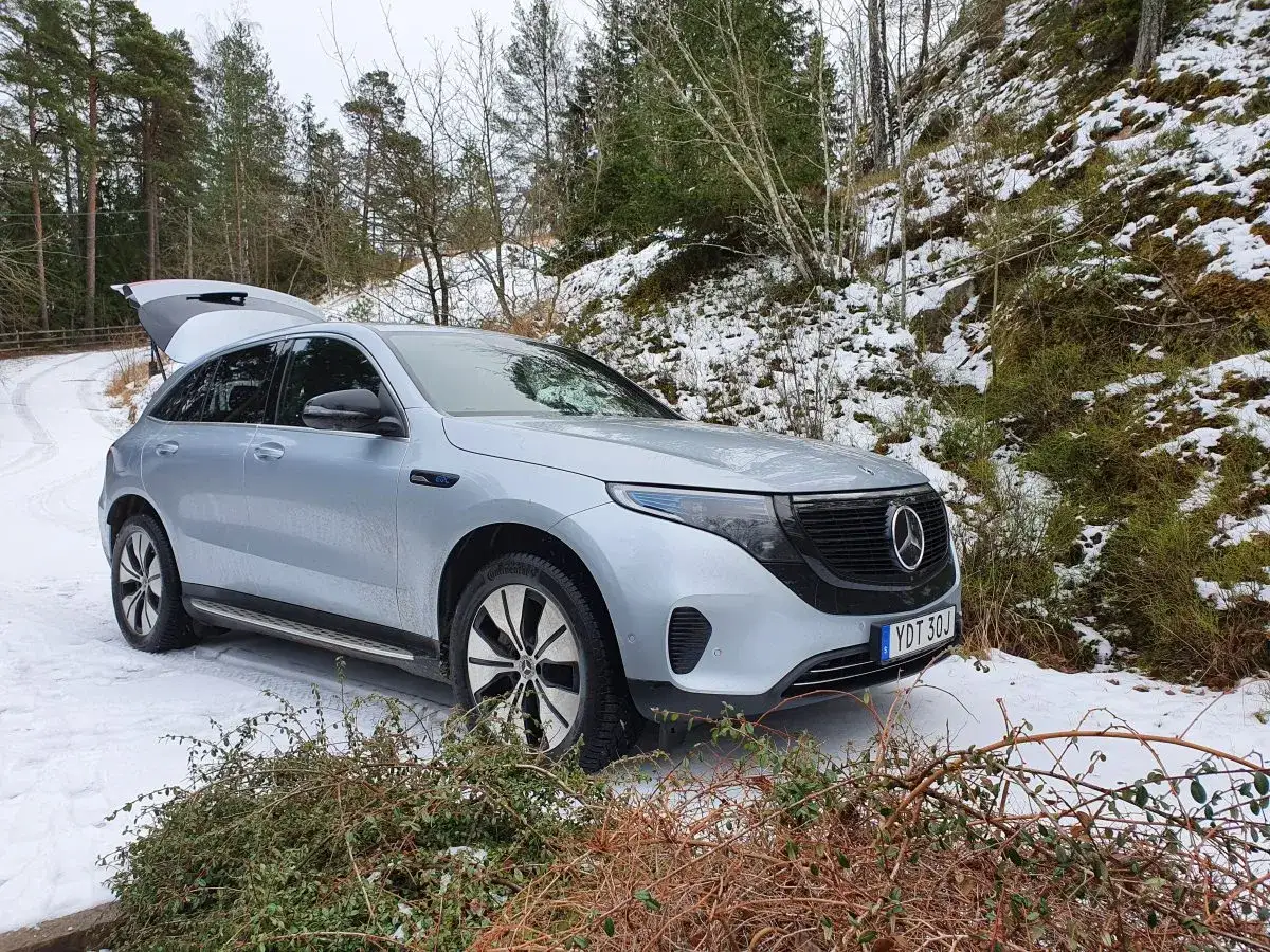 En silverf&auml;rgad EQC Mercedes st&aring;r parkerad p&aring; en sn&ouml;ig skogsv&auml;g i Sverige. Bagageluckan &auml;r &ouml;ppen.