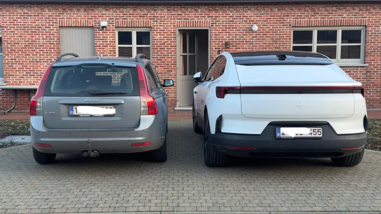 En grå Volvo V50 står bredvid en vit Polestar. Båda bilarna är parkerade på en uppfart framför ett tegelhus.