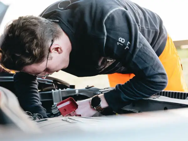 Man med glasögon böjd över bilmotorn, kanske för att fixa det brummande ljudet från bilen.
