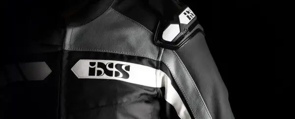 Detaljer på en svart och grå ixs motorcykeljacka med vita logotyper.