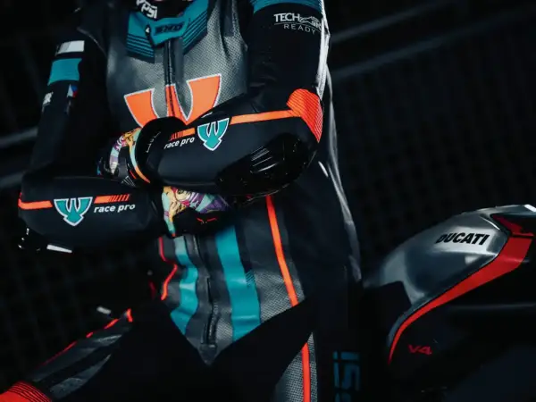 En förare i ett berik skinnställ med orange och turkosa detaljer sitter på en Ducati V4.