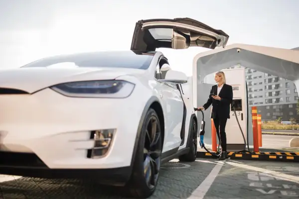 Kvinna laddar elbilen gratis vid laddstation. Bilen har uppfällda dörrar.
