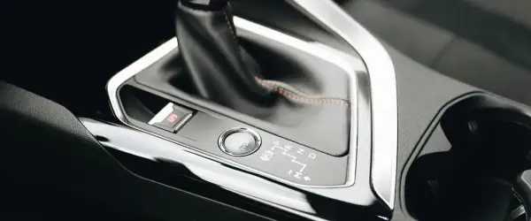 Detaljer från en bilinteriör: automatlådans växelspak, startknapp och parkeringsbroms. Dags att byta olja automatlåda för smidig körning.