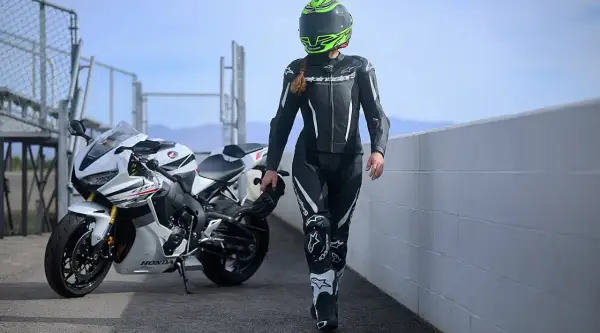 En förare i skinnställ går bredvid en vit Honda. Skinnställ storleksguide hjälper dig hitta rätt passform för din körning.