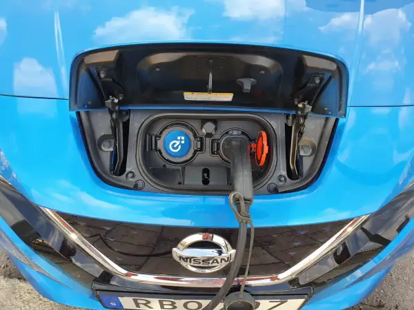 Blue Nissan Leaf with charging port open and cable plugged in.