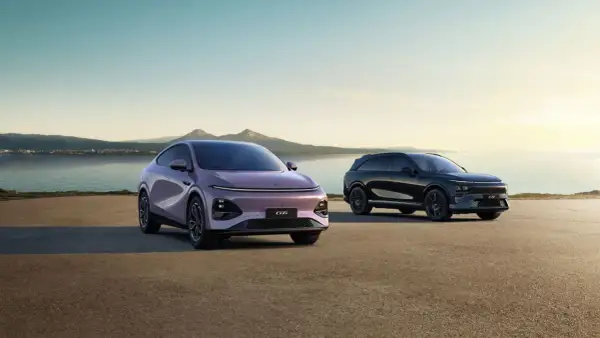 Två XPeng SUV:ar, en lila och en svart, står vid en sjö med berg i bakgrunden.